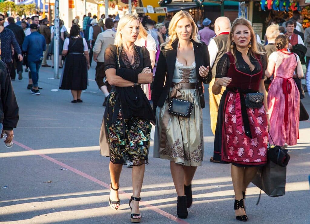 Three women wearing traditional clothing walking through Oktoberfest grounds